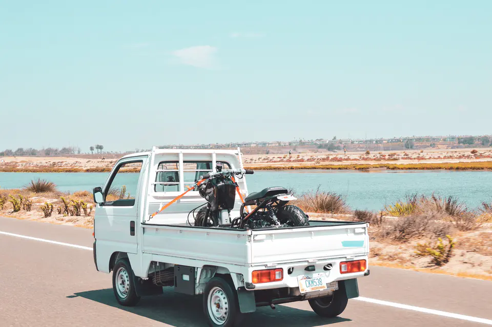 White Honda Acty Kei Truck hauling a dirt bike on a coastal road